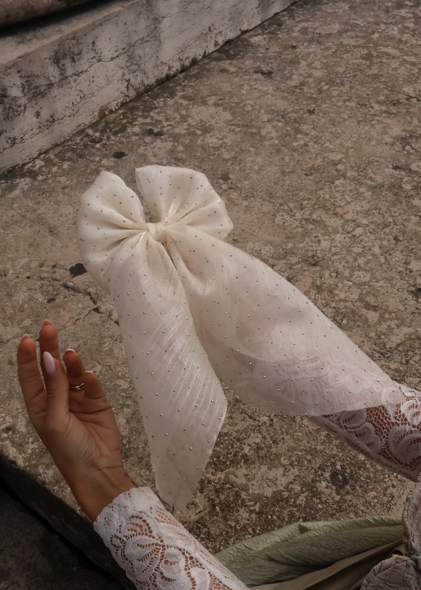 White lace bow on a concrete surface with a hand holding it.
