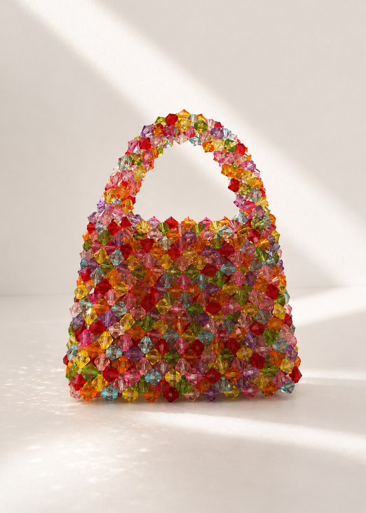 A structured handbag covered in colorful faceted crystal-like embellishments, photographed on a clean white studio background with soft diagonal shadows.