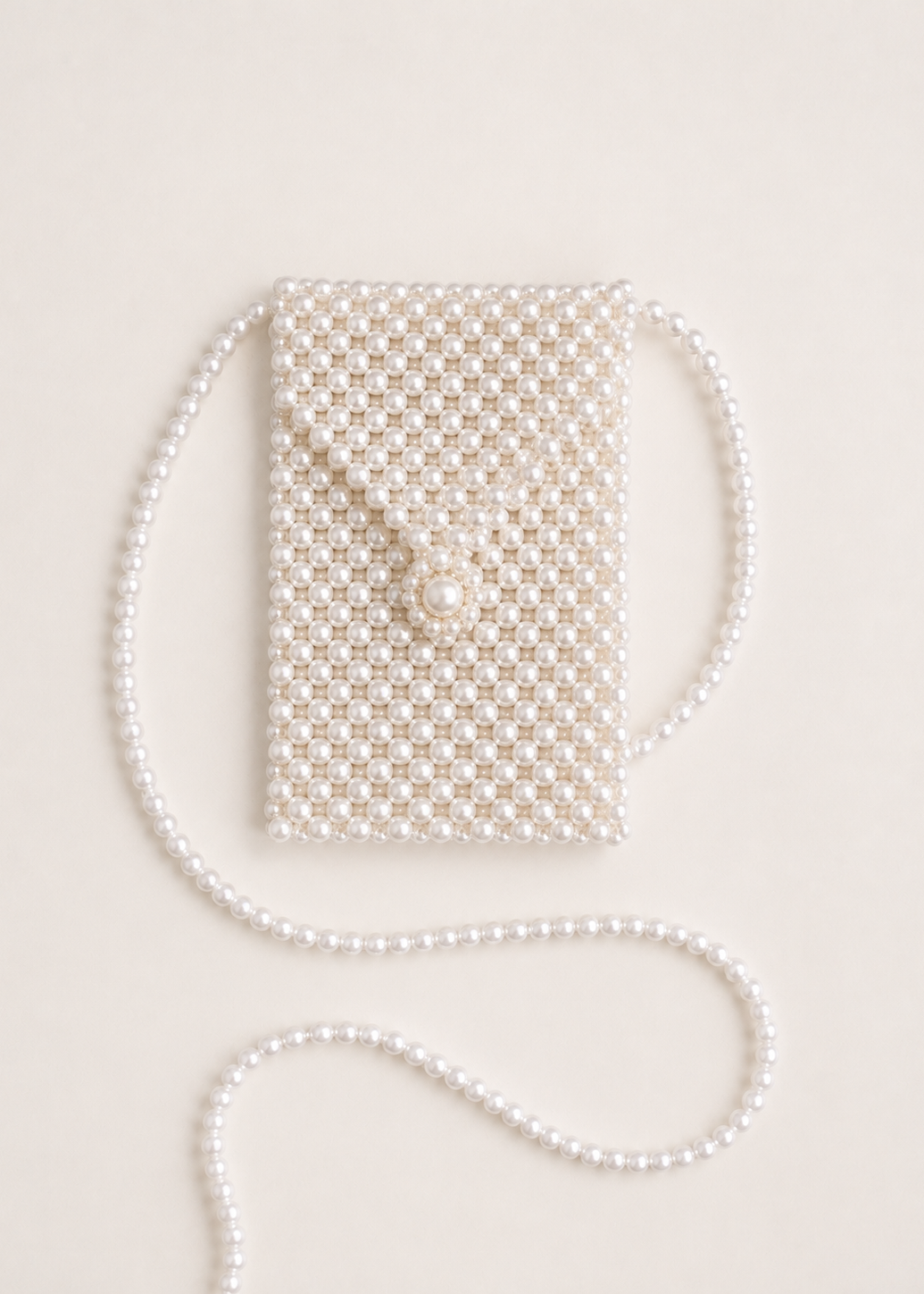 A small pearl-beaded clutch bag with a matching pearl strap, laid flat on a light cream background.
